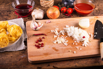 Cooking fettuccine pasta with tomato, onion, garlic and hot pepper sauce - Sliced onion and garlic on the table with ingredients
