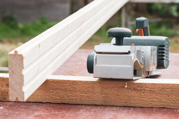 processes boards with an electric plane, preparing the surface of wood, leveling the boards with an...
