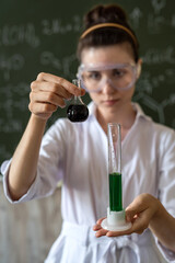 student in white coat and glasses holds a flask in his hands and conducts an experiment