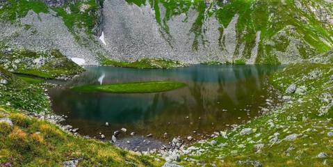 shallow clear mountain lake with many stones at the shore panorama