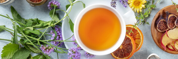 Tea panorama with herbs, flowers and fruit, shot from above. Healthy hot drink panoramic banner with orange
