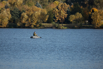 Fototapeta na wymiar Fisherman in a rubber boat on an autumn lake. Fishing boat. Landscape with a boat and a fisherman on the lake in autumn.