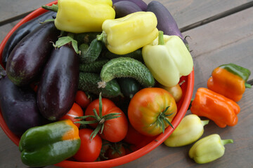A set of fresh vegetables from your garden. Eggplant, pepper, tomatoes, cucumbers in a red bowl on a wooden background.