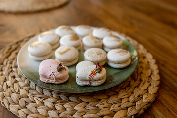 White and pink macarons lie on a plate on a wooden table. Delicious light cookies on a brown background. Bakery
