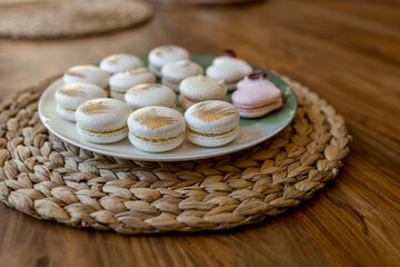 White and pink macarons lie on a plate on a wooden table. Delicious light cookies on a brown background. Bakery