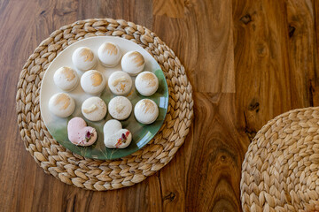White and pink macarons lie on a plate on a wooden table. Delicious light cookies on a brown background. Bakery