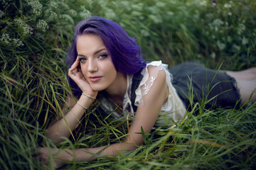 Naklejka na ściany i meble portrait of a teenage girl with purple hair and an earring in her nose lying in the grass
