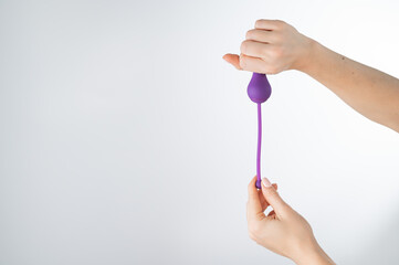 A faceless woman holding an electronic Kegel trainer for training pelvic floor muscles on a white background. Sex toy synchronized with a smartphone