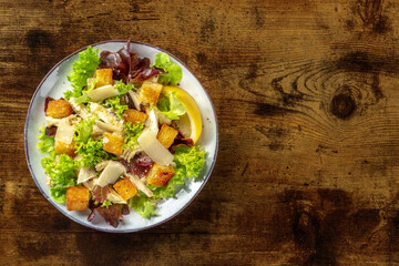 Chicken Caesar salad, shot from above on a dark rustic wooden background. Lettuce, croutons, chicken fillet meat and the classic dressing