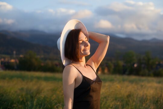 woman standing in a field, holding hat and looking at sun, space for text, atmospheric epic moment