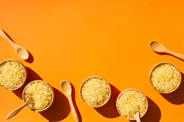 Wooden spoons and bowls filled with yellow bath sea salt. Beauty treatment for spa and wellness. Skincare natural cosmetic concept for body care. Top view on orange background. Place for text