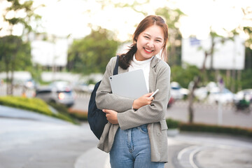 Female college students happily holding laptops outdoors after school on campus. when the sun goes down the horizon with warm light