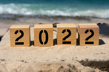 wooden cube written 2022 on the beach sand.