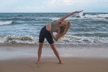 Sporty fit active sexy young woman in sportswear stretching on the beach. Female healthy girl do sport gymnastics workout exercise outdoors by the sea