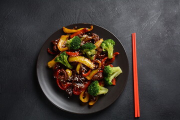 Asian teriyaki beef with red and yellow bell peppers, broccoli and sesame seeds on a plate on the...