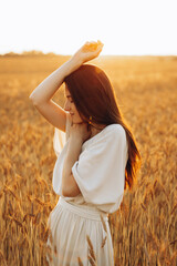 Attractive Ukrainian girl with dark long hair, slender and beautiful posing for a photo in a yellow sunny field with wheat