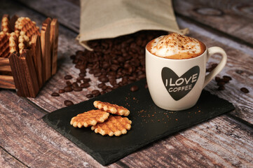 Cup of coffee with milk accompanied by small cookies with coffee beans on wooden table
