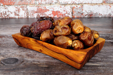 Group of ripe soft and sticky medjool and zamli dates in an olive wood serving dish