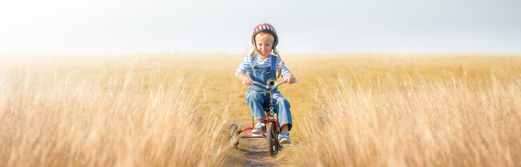 Little boy rides a bicycle. A cheerful, happy child imagines himself a cyclist and plays outdoors against a blue sky on a summer day. Games, dreams of competition in retro style.