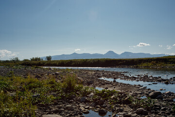 A clear river with rocks leads to the mountains. Clear summer day. Wildlife travel concept.