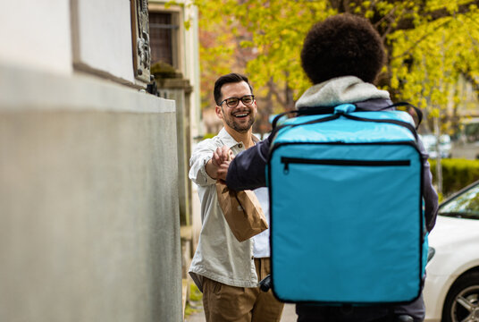 Male courier with bicycle delivering fast food to the customer in city.