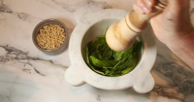 Pesto alla genovese. Genoese pesto, typical Italian sauce.Preparation of Genoese pesto in the typical Carrara marble mortar with basil leaves, pine nuts, olive oil, Parmesan cheese and salt. Italy. 