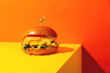 Big burger with cheese on bright orange and yellow background. American Fast food cuisine in a modern style.