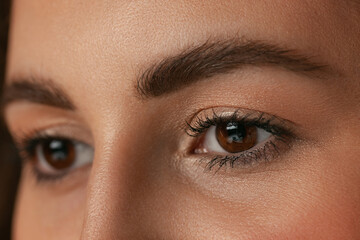 Naklejka premium Close-up image of female brown eyes without makeup isolated over dark studio background. Natural beauty concept.