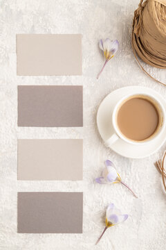 Gray paper business card mockup with spring snowdrop crocus flowers and cup of coffee on gray concrete background. top view, copy space.
