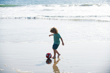 Little boy child play football on coast of sea beach. Summer kids sports.