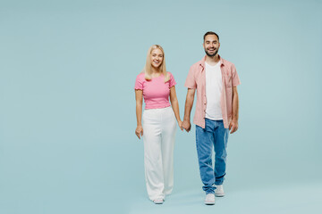 Fototapeta premium Full body length young smiling happy cheerful couple two friends family man woman in casual clothes looking camera hold hands together isolated on pastel plain light blue background studio portrait.
