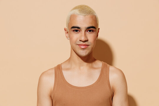 Young smiling happy blond latin american hispanic gay man 20s with make up in beige tank shirt looking camera isolated on plain light ocher background studio portrait People lgbt lifestyle concept
