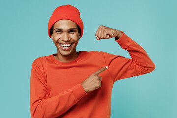 Young fun african american man in red shirt hat show point finger on biceps muscles on hand...