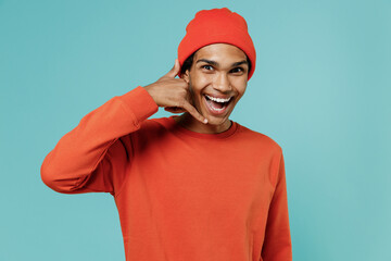 Fototapeta premium Young cheerful fun cool smiling happy african american man in red shirt hat doing phone gesture like says call me back isolated on plain pastel light blue background studio. People lifestyle concept