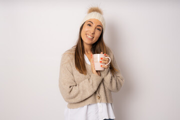Cheerful young woman wearing winter clothing standing isolated over white background, holding a cup