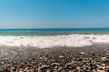 Fototapeta na wymiar View of Aphrodite Beach. Afternoon at the sea. Bright sun, foam from the wave, pebble beach. Large stones on the beach, beautiful sea view. Legends of Greece. Aphrodite.