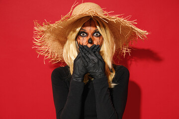 Young shocked amazed woman with Halloween makeup mask wears straw hat black scarecrow costume cover mouth with hand isolated on plain red background studio portrait. Celebration holiday party concept.