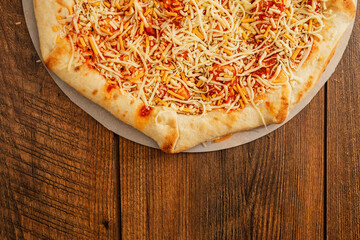 Simple cheese pizza on a cardboard base on a wooden table surface. Frozen product. Italian style fast food.