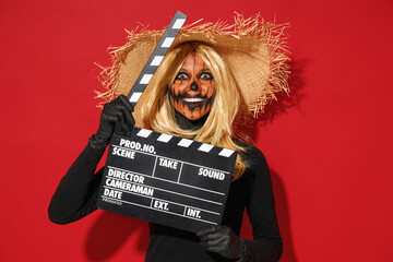 Young woman with Halloween makeup mask wears straw hat black scarecrow costume holding classic black film making clapperboard isolated on plain red background studio Celebration holiday party concept - obrazy, fototapety, plakaty