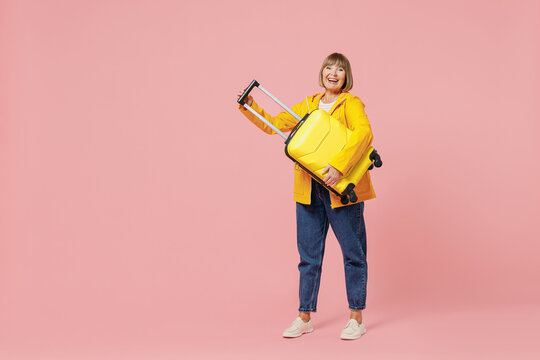 Full Size Body Length Traveler Tourist Mature Elderly Woman 55 Years Old Wear Casual Clothes Hat Scarf Hold Carry Suitcase Bag Under Hand Isolated Plain Pastel Light Pink Background Studio Portrait