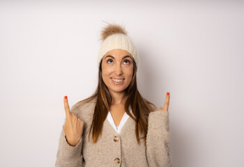 Young brunette woman wearing winter clothing over white background surprised looking up and pointing with fingers.