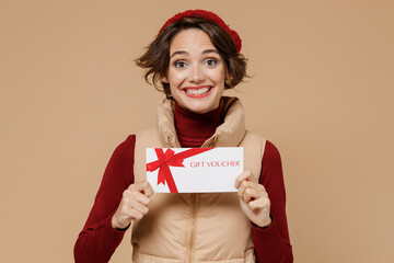 Young smiling happy woman 20s wears red turtleneck vest beret hold gift certificate coupon voucher...
