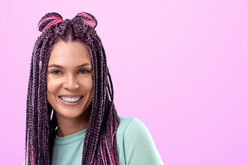 Beautiful girl with a hairstyle of pink braids in turquoise clothes smiles and poses on a pink background in the studio. The concept is modern style, individuality, inclusiveness, creativity.