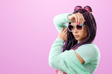 Beautiful girl with a hairstyle of pink braids in turquoise clothes and sunglasses posing on a pink...