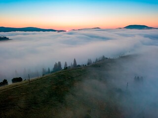 Fog spreads over the mountains at dawn. The sun rises on the horizon. Ukrainian Carpathians in the morning. Aerial drone view.