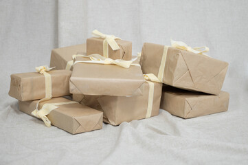 Bunch of Christmas gifts in boxes wrapped in brown kraft paper and tied with silk ribbons on linen fabric background