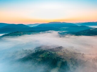 Fog spreads over the mountains at dawn. The sun rises on the horizon. Ukrainian Carpathians in the morning. Aerial drone view.