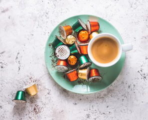 Used coffee capsules on a green plate with a coffee cup on a weathered white table. Recyclable...
