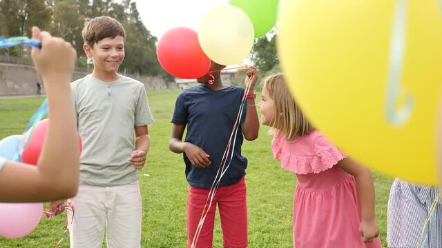 Group of boys and girls playing on field with multicolored balloons.