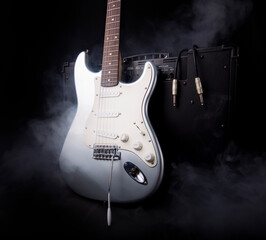 Silver electric guitar and guitar amplifier in smoke on black background.